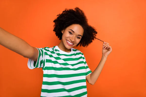 Självporträtt av attraktiva glada vågiga hår flicka vidröra lockar isolerade över levande orange färg bakgrund — Stockfoto