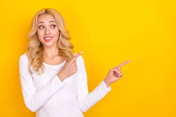 Foto de mujer joven sospechosa divertida usar camisa blanca morder labio apuntando espacio vacío aislado color amarillo fondo — Foto de Stock
