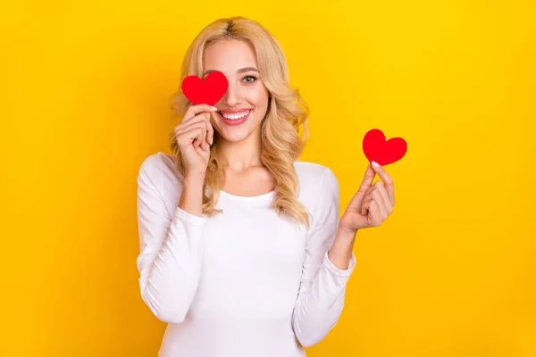 Photo of adorable cute young woman wear white shirt holding little hearts cover eye isolated yellow color background — Fotografia de Stock