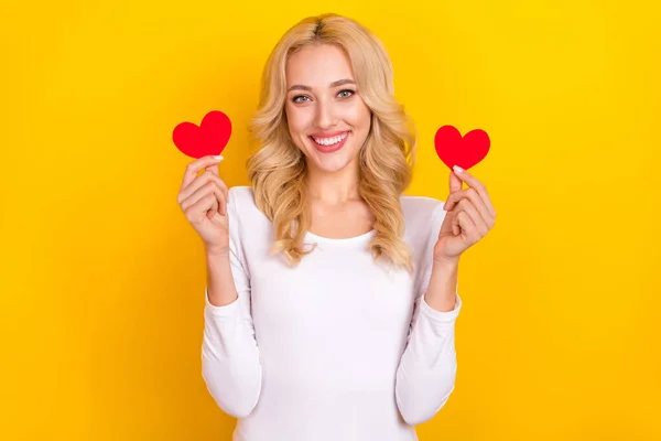 Foto de mulher muito adorável jovem usar camisa branca segurando dois corações pequenos isolado cor amarela fundo — Fotografia de Stock