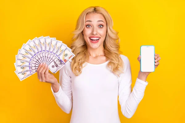 Photo of impressed young blond lady hold telephone money wear white shirt isolated on yellow color background — Foto Stock
