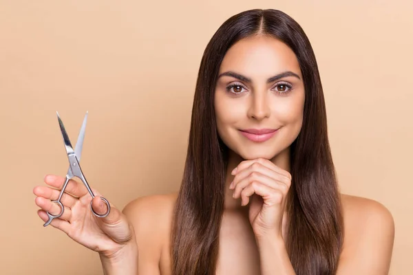 Portrait of attractive cheery confident long-haired girl holding scissors making decision isolated over beige pastel color background — Stockfoto
