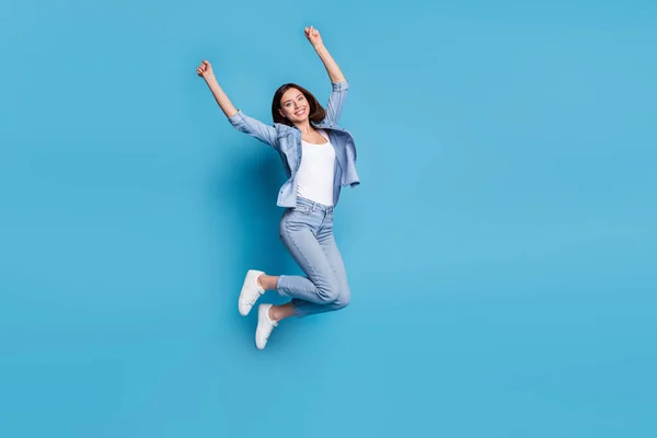 Foto de doce senhora sortuda vestida camisa jeans levantando punhos saltando alto isolado fundo cor azul — Fotografia de Stock