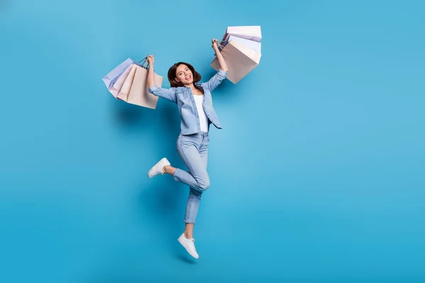 Foto di brillante bella signora vestita camicia di denim salto alto tenuta borse della spesa isolato sfondo di colore blu — Foto Stock
