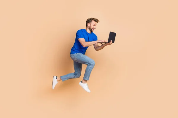 Full size profile side photo of young energetic guy type chat laptop jump up agent isolated over beige color background — Photo