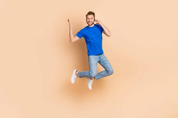 Full length photo of young man jump up tell listen talk mobile communication energy isolated over beżowy kolor tła — Zdjęcie stockowe