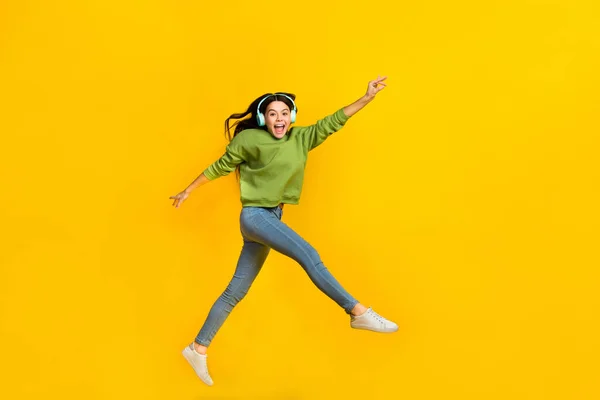 Full body profile side photo of young excited girl jump walk listen music earphones energetic isolated over yellow color background —  Fotos de Stock