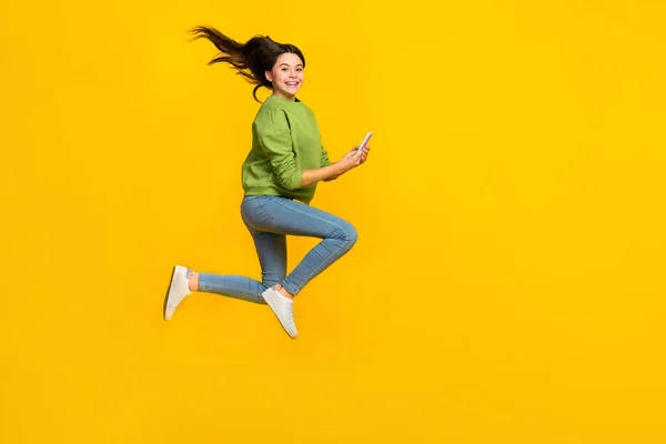 Foto lateral de perfil de cuerpo completo de niña salto enérgico uso móvil compartir aplicación aislado sobre fondo de color amarillo —  Fotos de Stock