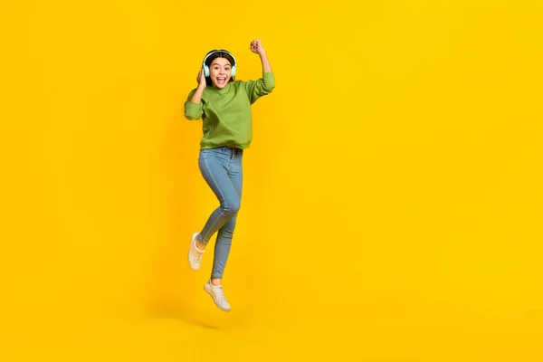 Full length photo of young active girl celebrate luck success triumph jump up listen radio isolated over yellow color background — Stok fotoğraf