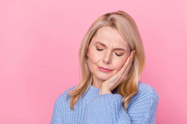 Photo of pain mature blond lady hand cheek wear blue sweater isolated on pink color background — стоковое фото