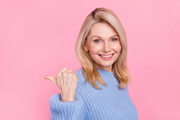 Фото зрелой милой блондинки указывает на промо носить синий пуловер изолированы на розовом фоне — стоковое фото