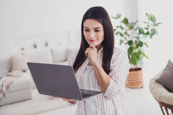 Portrait of attractive focused long-haired woman using laptop reading document presentation at home indoors — Zdjęcie stockowe