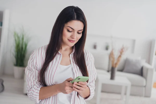 Portrait of attractive focused long-haired woman using device chatting using web app at home indoors — стоковое фото