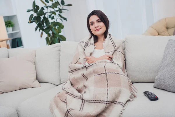 Портрет привабливої спокійної веселої жінки, що сидить на дивані, покритому теплою ковдрою, дивиться телевізійне шоу вдома в приміщенні — стокове фото