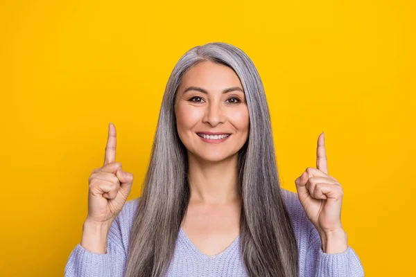 Foto de bonito encantador aposentado mulher usar camisola azul apontando para o espaço vazio isolado cor amarela fundo — Fotografia de Stock