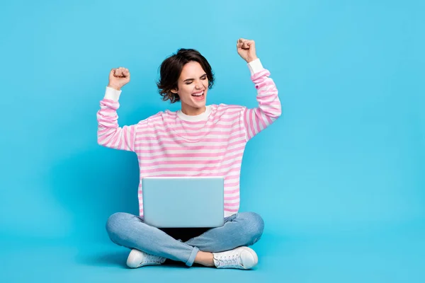 Photo of ecstatic pretty girl raise fists in victory achievement sit floor with laptop isolated on blue color background — Stock Photo, Image