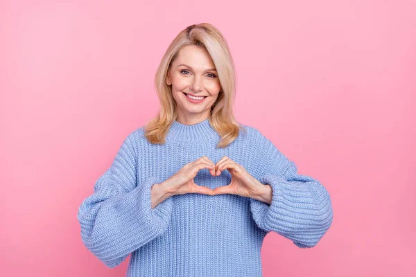 Foto de señora rubia optimista madura manos corazón desgaste suéter azul aislado sobre fondo de color rosa — Foto de Stock