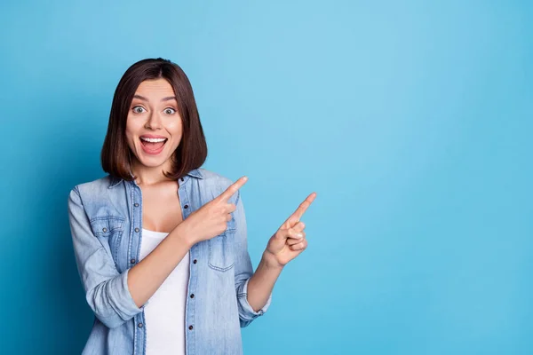 Photo of excited sweet lady dressed denim shirt pointing two fingers empty space isolated blue color background — Foto Stock