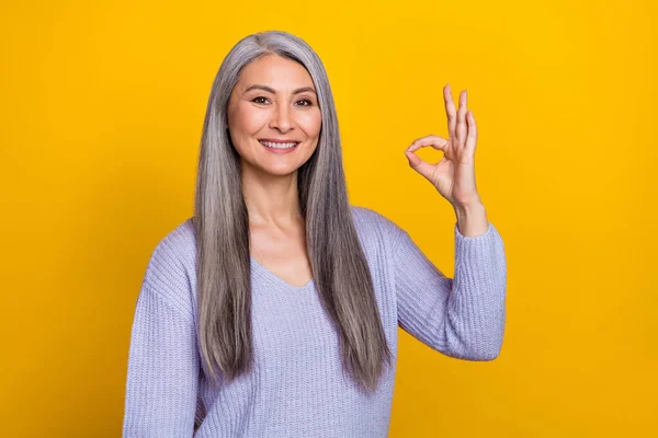 Photo of charming cheerful mature woman in knitted jumper showing okay symbol advert isolated on yellow color background —  Fotos de Stock