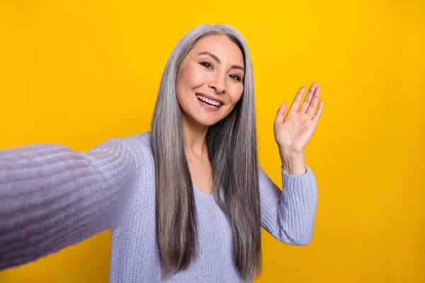 Portrait of adorable cheerful grandma make video vlog about her journey trip wave hand say hi isolated on yellow color background — Stock Fotó