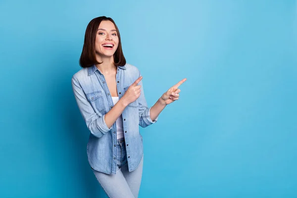 Photo of shiny excited woman wear jeans shirt smiling pointing empty space isolated blue color background — 스톡 사진