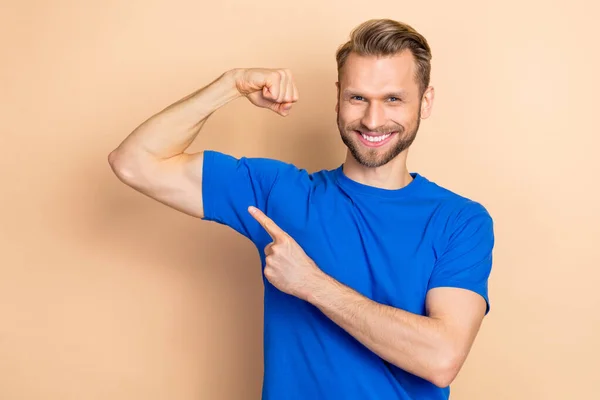 Foto de alegre hombre confiado brazo de dedo directo que muestra bíceps aislados sobre fondo de color beige — Foto de Stock