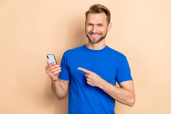 Photo of young man indicate finger mobile app download button recommend select isolated over beige color background — Stok fotoğraf