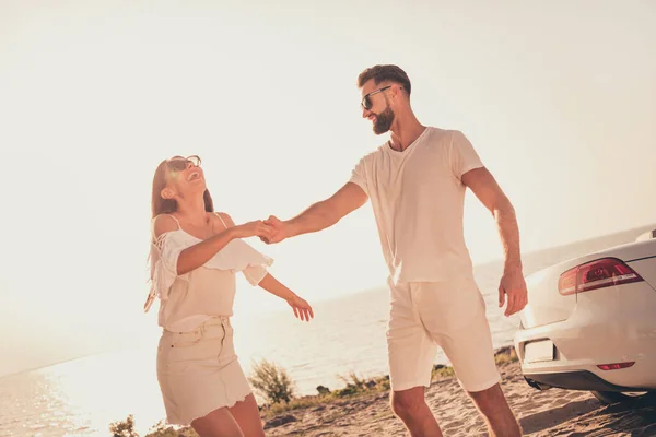 Foto de pareja casada bastante alegre vestida ropa blanca conduciendo coche caminando playa sosteniendo brazos al aire libre país lado de la carretera —  Fotos de Stock