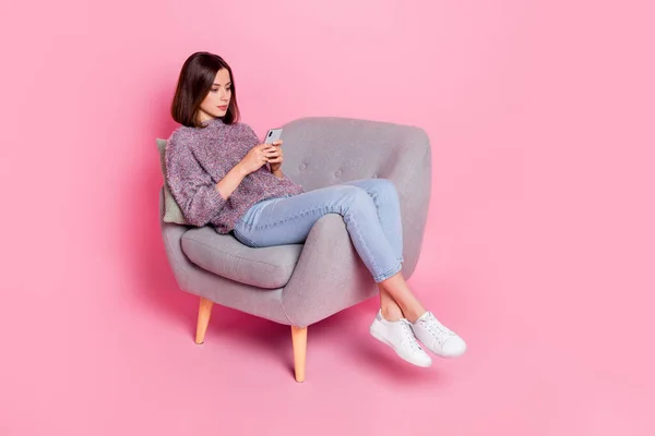 Photo of shiny serious lady dressed sweater sitting chair typing modern device isolated pink color background — Fotografia de Stock