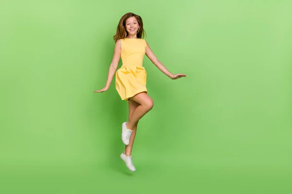 Full size photo of sweet jumping casual wear girl wear cute yellow dress spring vacation isolated on green color background — стоковое фото