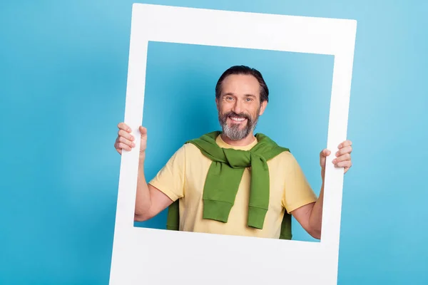 Porträt von fröhlichen Mann halten Papier Fotokarte zahmes Lächeln suchen Kamera isoliert auf blauem Hintergrund — Stockfoto