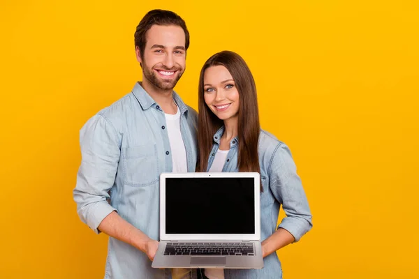 Portrait of handsome beautiful cheerful couple holding laptop copy blank space isolated over bright yellow color background — Zdjęcie stockowe