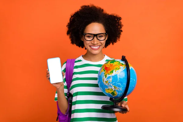 Portrait of beautiful trendy cheerful girl holding globe find point place tour using device gps isolated on bright orange color background — ストック写真