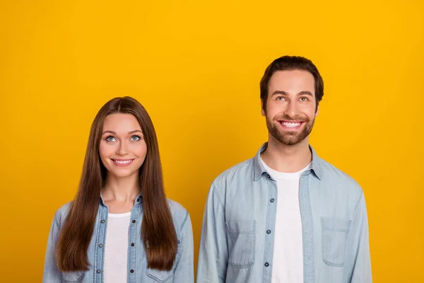 Foto de fresco milenar casal penteado marrom olhar para cima desgaste jeans camisas isoladas no fundo amarelo — Fotografia de Stock