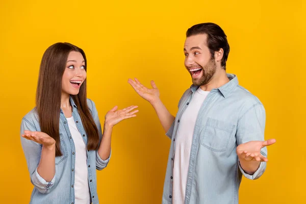 Foto de impressionado jovem casal penteado marrom dizer usar camisas jeans isoladas no fundo amarelo — Fotografia de Stock