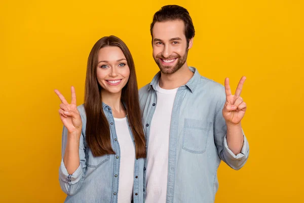 Photo of funny cheerful husband wife wear jeans shirts showing v-signs isolated yellow color background —  Fotos de Stock