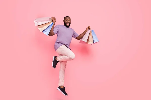 Fotografie vzrušený cool chlap oblečený fialové tričko skákání vysoké stoupající nakupující izolované růžové barvy pozadí — Stock fotografie