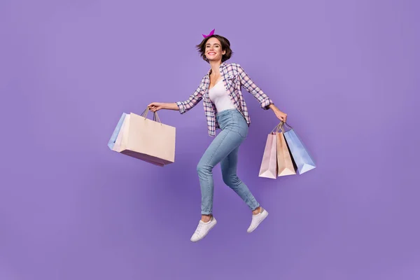Foto van haasten zoete dame gekleed geruite shirt springen hoge holding koopjes geïsoleerde paarse kleur achtergrond — Stockfoto