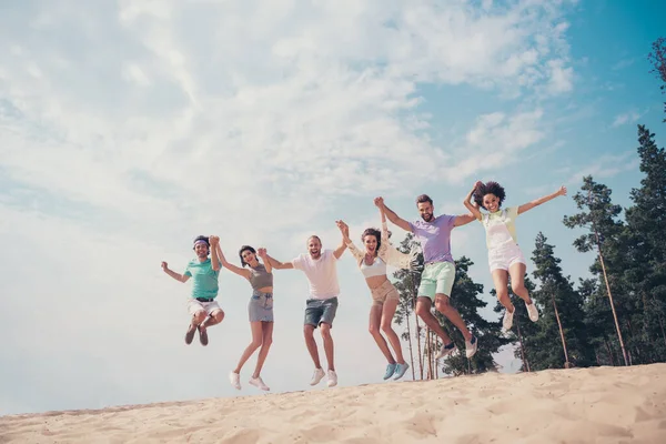 Photo of positive cheerful friends hold hands jump enjoy flight wear casual outfit nature summer seaside beach —  Fotos de Stock