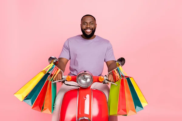 Photo of funny cheerful guy wear purple t-shirt riding moped carrying shoppers isolated pink color background — Stock fotografie