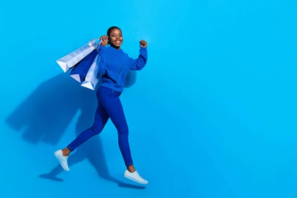 Photo of sweet lucky woman wear sweatshirt jumping rising shoppers empty space isolated blue color background — Fotografia de Stock