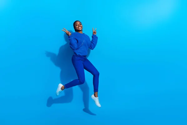 Foto de mulher brilhante animado usar camisola saltando mostrando v-sinal espaço vazio isolado azul cor de fundo — Fotografia de Stock
