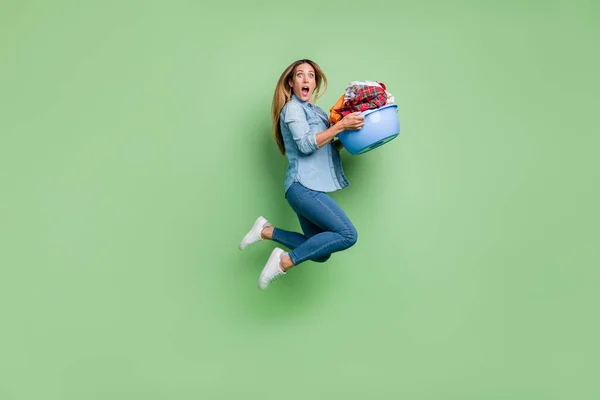 Full length profile photo of young lady jump wash cloth wear shirt jeans shoes isolated on green background — Stockfoto