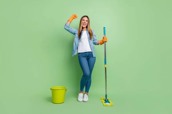Full body photo of mature cool lady clean floor yell wear shirt jeans shoes gloves isolated on green background — Fotografia de Stock
