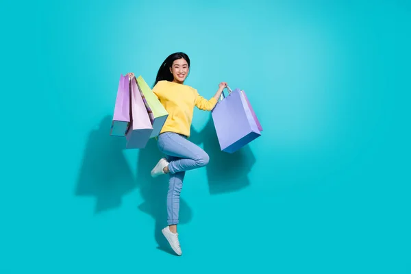 Full length photo of excited sweet lady dressed yellow sweater jumping holding shoppers empty space isolated turquoise color background — 스톡 사진