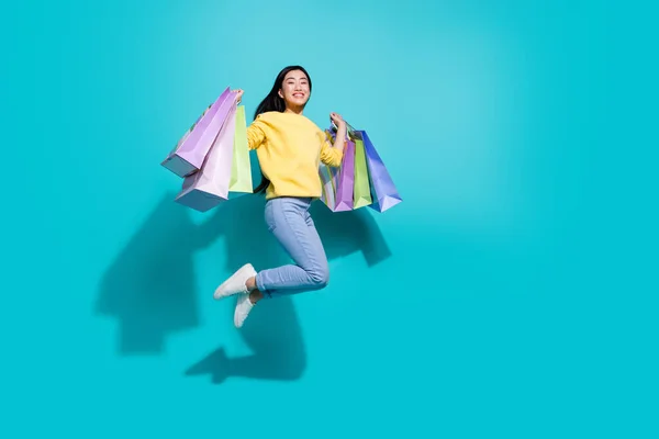 Full length photo of sweet pretty lady dressed yellow sweater jumping rising shoppers empty space isolated turquoise color background — Stockfoto