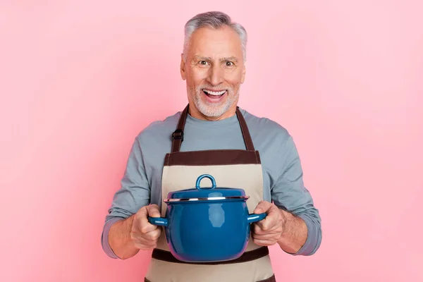 Fénykép izgatott csinos nyugdíjas férfi viselni szürke ing kötény főzés ízletes vacsora elszigetelt rózsaszín szín háttér — Stock Fotó
