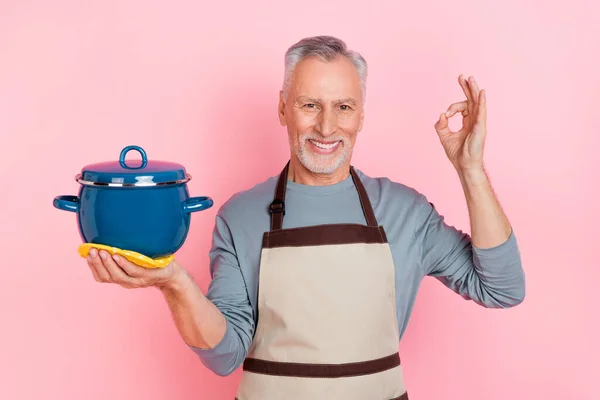 Photo of funny sweet man pensioner dressed grey shirt apron holding saucepan okey sign isolated pink color background — Stok fotoğraf