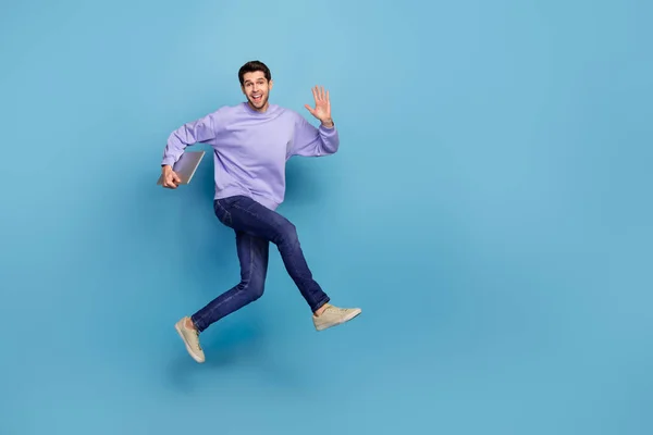 Повнорозмірний вигляд тіла привабливого веселого хлопця, який стрибає з ноутбуком, махаючи привіт, ізольований на яскраво-синьому кольоровому фоні — стокове фото