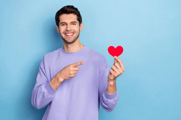 Retrato de atractivo chico alegre demostrando tarjeta de corazón 14 Febrero aislado sobre fondo de color azul brillante — Foto de Stock